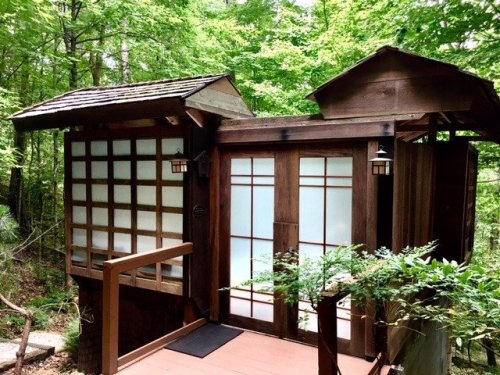 A wooden cabin with sliding glass doors, surrounded by lush green trees in a serene forest setting.