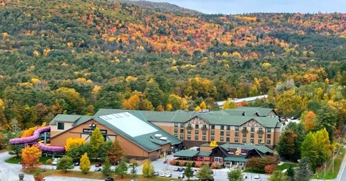 A large hotel surrounded by vibrant autumn foliage and rolling hills, with a water slide visible on the side.