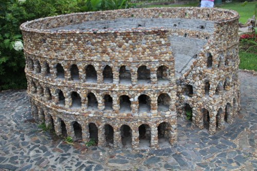 A miniature stone replica of the Colosseum, featuring detailed arches and a circular design, set on a stone pathway.