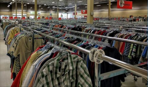 A wide view of a clothing store aisle filled with racks of assorted shirts in various colors and patterns.