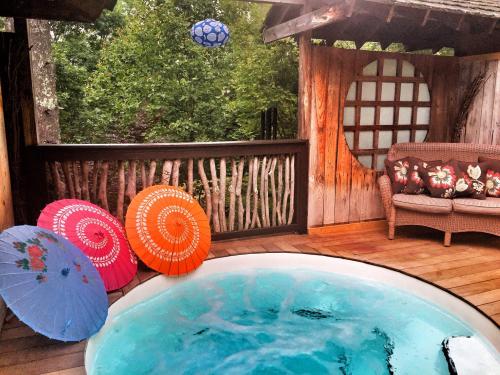 A cozy outdoor space featuring a hot tub, colorful umbrellas, and a wooden deck surrounded by greenery.