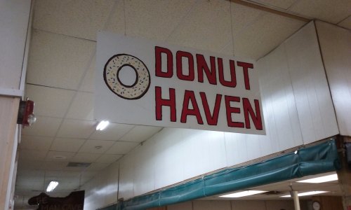 Sign for "Donut Haven" with a donut graphic, hanging in a brightly lit indoor space.