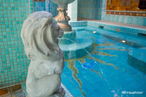 A stone lion statue spouts water into a turquoise tiled pool, surrounded by decorative tiles and a fountain.