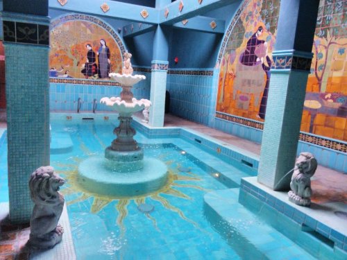 A serene indoor pool with a central fountain, surrounded by colorful murals and lion statues.