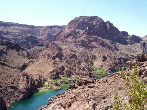 A scenic view of rugged mountains surrounding a winding river under a clear blue sky.