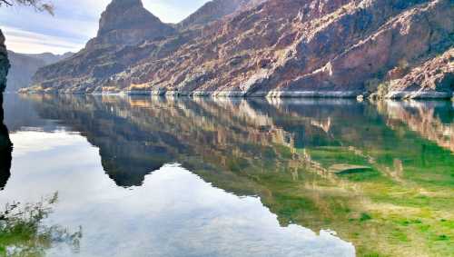 A serene lake reflecting rocky mountains and clear blue skies, surrounded by lush greenery.