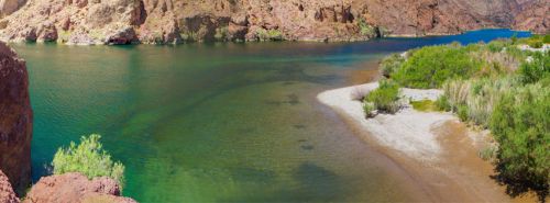 A serene river scene with clear green water, sandy shores, and lush vegetation surrounded by rocky cliffs.