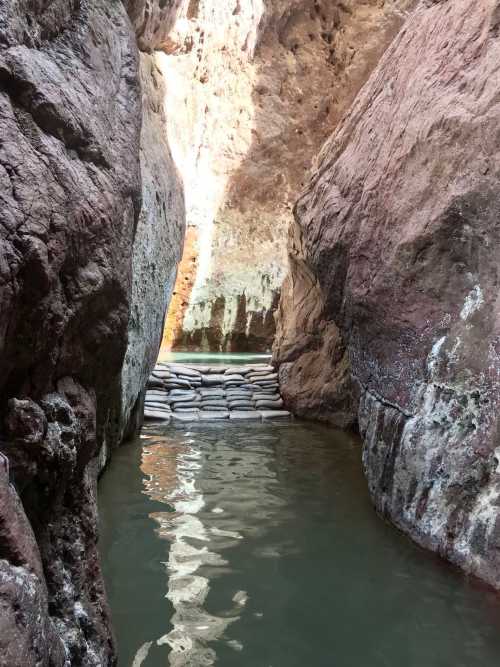 Narrow canyon with steep rock walls and calm water, featuring a sandbag barrier in the foreground.