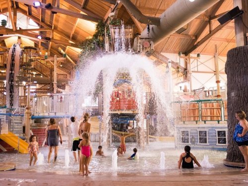 A lively indoor water park with children and adults enjoying water slides and a large splash feature.
