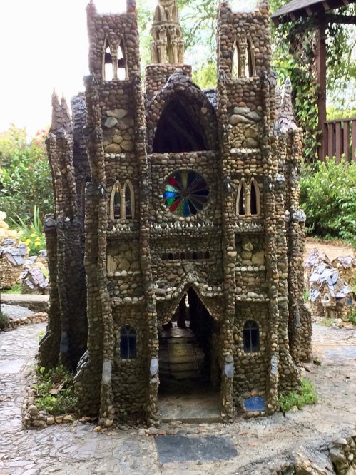 A whimsical stone structure resembling a castle, featuring intricate details and a colorful stained glass window.