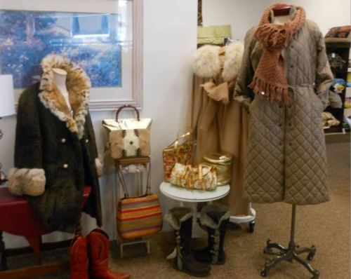A display of winter fashion featuring coats, scarves, boots, and accessories in a cozy boutique setting.