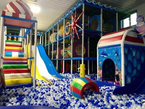 Colorful indoor play area featuring slides, climbing structures, and a ball pit filled with blue and white balls.