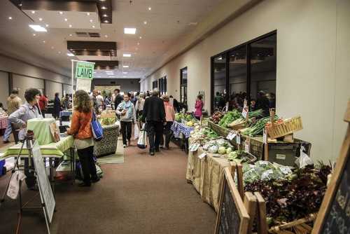 A bustling indoor market with vendors selling fresh produce and goods, and shoppers browsing the stalls.