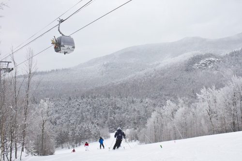 Skiers on a snowy slope with a gondola overhead and mountains in the background, all covered in frost.