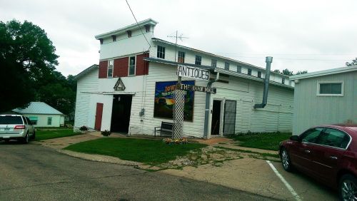 A white building with a sign reading "Antiques," featuring a grassy area and parked cars nearby.