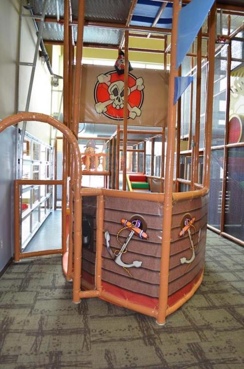 Indoor play area designed like a pirate ship, featuring climbing structures and colorful play equipment.