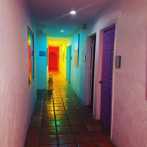 A brightly lit hallway with colorful walls and doors, featuring a caution sign on the tiled floor.