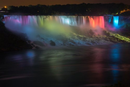 A vibrant display of colored lights illuminating Niagara Falls at night, reflecting on the water below.