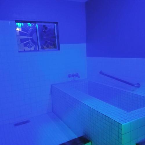 A dimly lit bathroom with blue lighting, featuring a tiled bathtub and a window with stained glass.