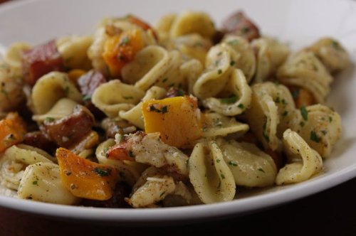 A close-up of a bowl of orecchiette pasta mixed with roasted vegetables and herbs.