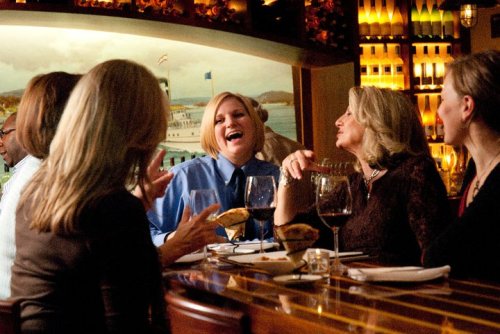 A group of friends enjoying dinner and wine at a restaurant, laughing and chatting together.