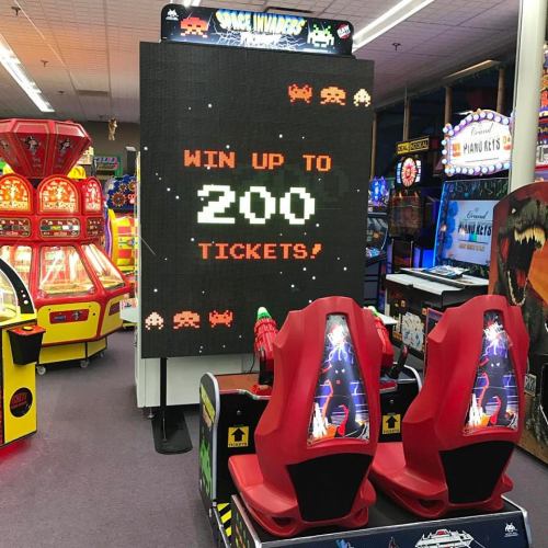 Arcade scene featuring a large screen displaying "Win up to 200 tickets!" with red racing seats in front.