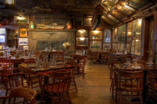 Cozy restaurant interior with wooden tables, chairs, and nautical decor, featuring warm lighting and a rustic atmosphere.