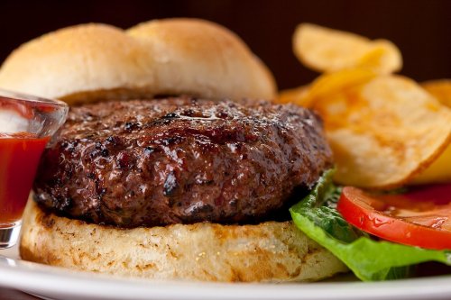 A juicy hamburger with lettuce, tomato, and a side of potato chips, served with a small dish of ketchup.