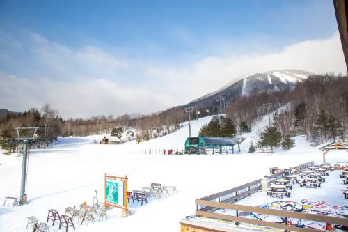 A snowy landscape with a ski lift, mountain in the background, and empty outdoor seating areas.