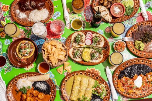 A vibrant table spread with various Mexican dishes, including tacos, enchiladas, rice, beans, and drinks.