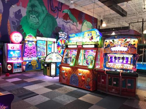 A colorful arcade with various games and bright lights, featuring a gorilla mural in the background.