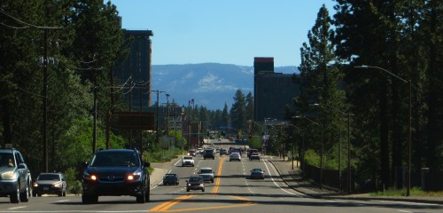 A wide road lined with trees, leading to buildings in the distance under a clear blue sky.