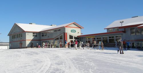 Ski resort building with people and equipment on a snowy slope under a clear blue sky.