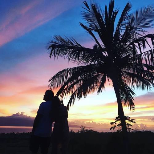 Silhouette of a couple standing under a palm tree against a vibrant sunset sky with pink and blue hues.