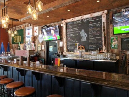 A rustic bar interior with wooden decor, a long counter, and screens displaying sports events.