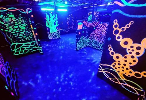 A vibrant, neon-lit maze with colorful, abstract designs on black walls, illuminated under UV light.