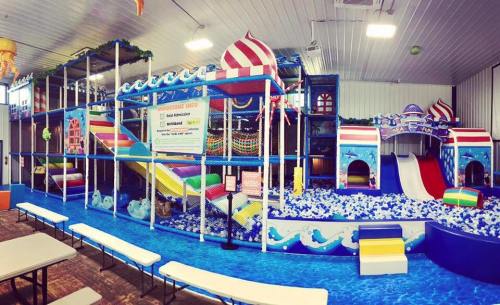 Colorful indoor water play area with slides, climbing structures, and a ball pit, surrounded by benches.