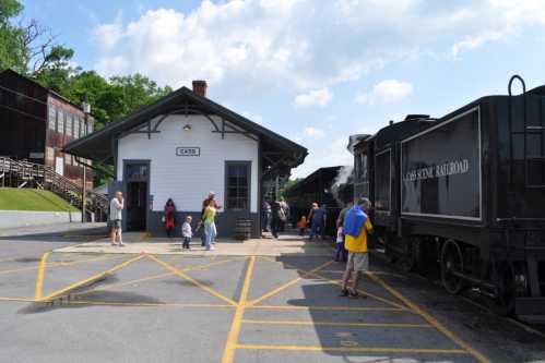 A historic train station with a steam locomotive, surrounded by people enjoying the day.