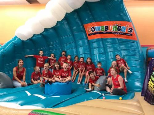 A group of children in red shirts poses on a large inflatable wave structure at a fun center.