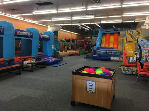 A colorful indoor play area featuring inflatable bounce houses, slides, and a ball pit with bright, soft balls.