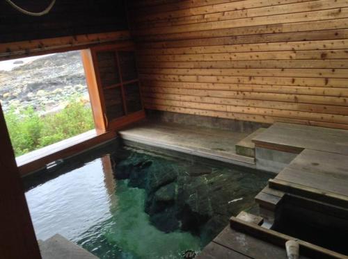 A serene wooden sauna with a stone hot spring, featuring a large window overlooking a natural landscape.