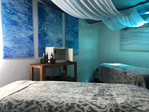 A serene spa room with two massage tables, blue abstract art on the walls, and soft draped fabric overhead.