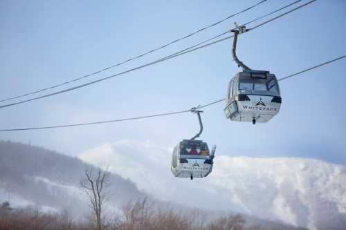 Two ski gondolas suspended on cables against a snowy mountain backdrop.