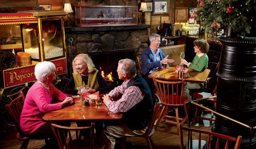 A cozy restaurant scene with four people at tables, enjoying drinks and conversation by a fireplace and a popcorn cart.