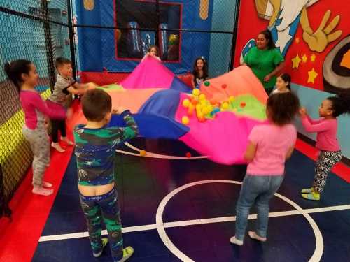 Children playing with a colorful parachute in a fun indoor play area, surrounded by bright walls and playful decorations.