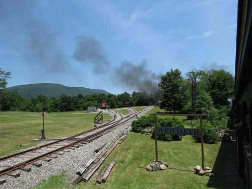 A train track curves through a green landscape, with smoke rising in the distance near a sign for Whittaker.