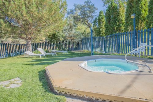 A small hot tub surrounded by green grass and lounge chairs, with a wooden fence and trees in the background.