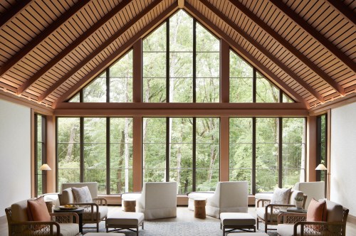 Bright, airy living room with large windows, wooden beams, and comfortable seating overlooking a lush green landscape.