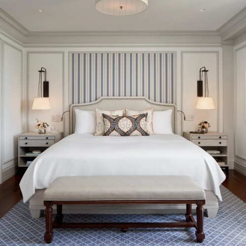 A stylish bedroom featuring a large bed with decorative pillows, a bench at the foot, and soft lighting.