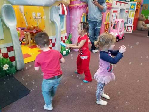 Three children play in a colorful indoor play area, surrounded by bubbles and toys, enjoying their time together.